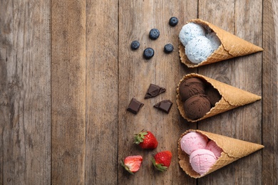 Photo of Flat lay composition with delicious ice creams in waffle cones on wooden table, space for text