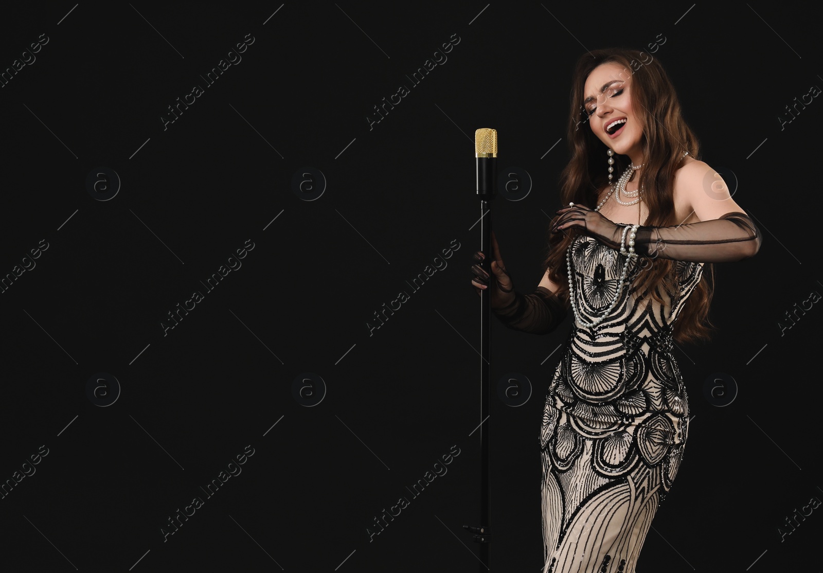 Photo of Beautiful young woman in stylish dress with microphone singing on black background