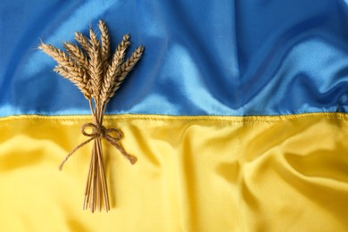 Photo of Bunch of wheat on Ukrainian national flag, top view. Space for text