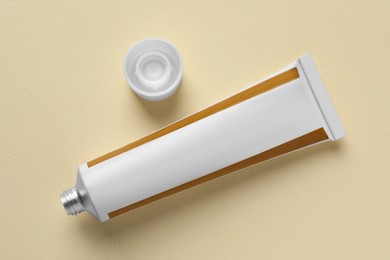 Open tube of ointment on beige background, flat lay. Space for text