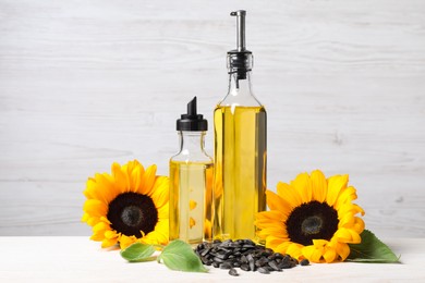 Photo of Bottles of sunflower cooking oil, seeds and yellow flowers on white wooden table