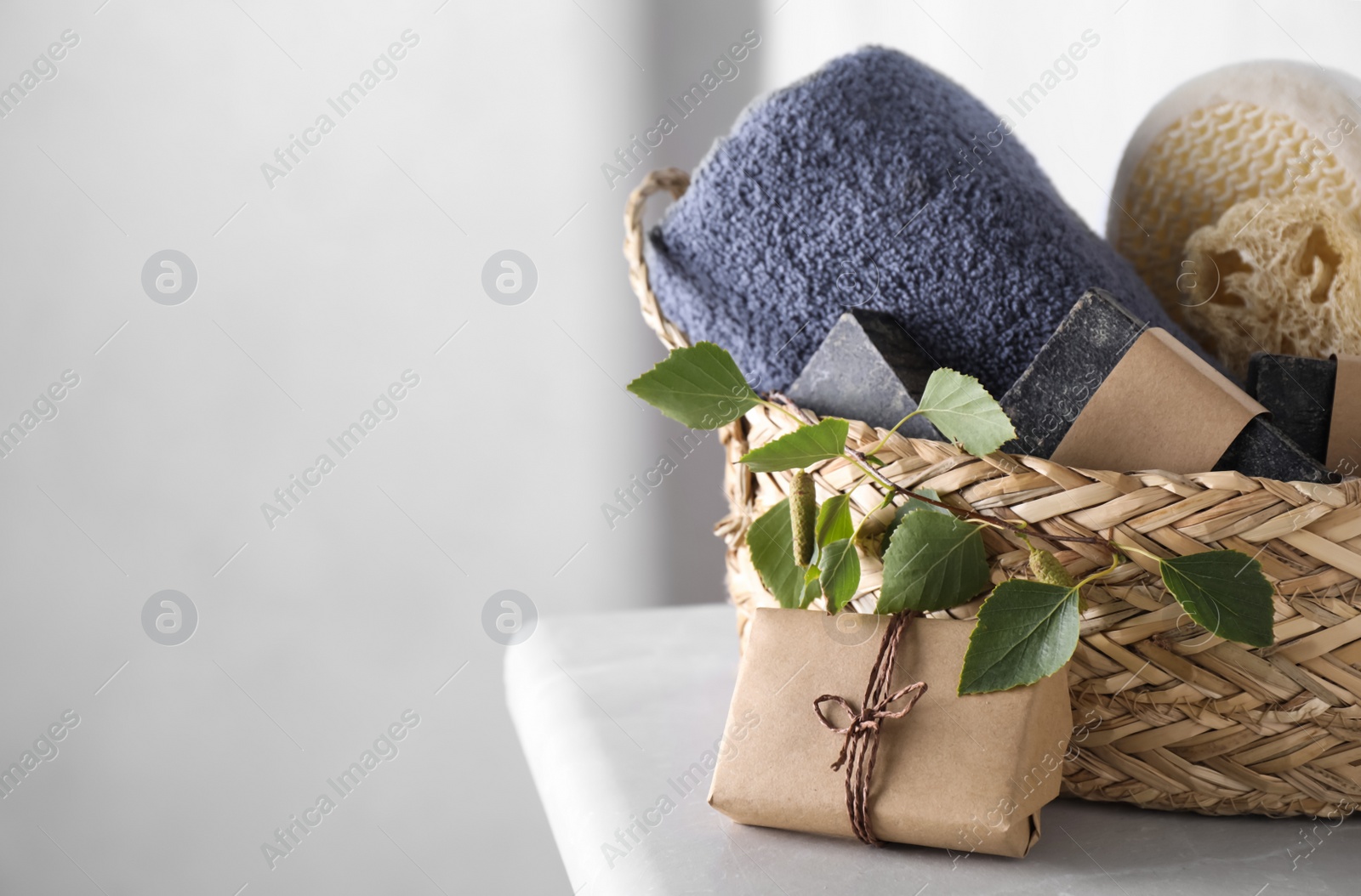 Photo of Natural tar soap and wicker basket on white table indoors. Space for text