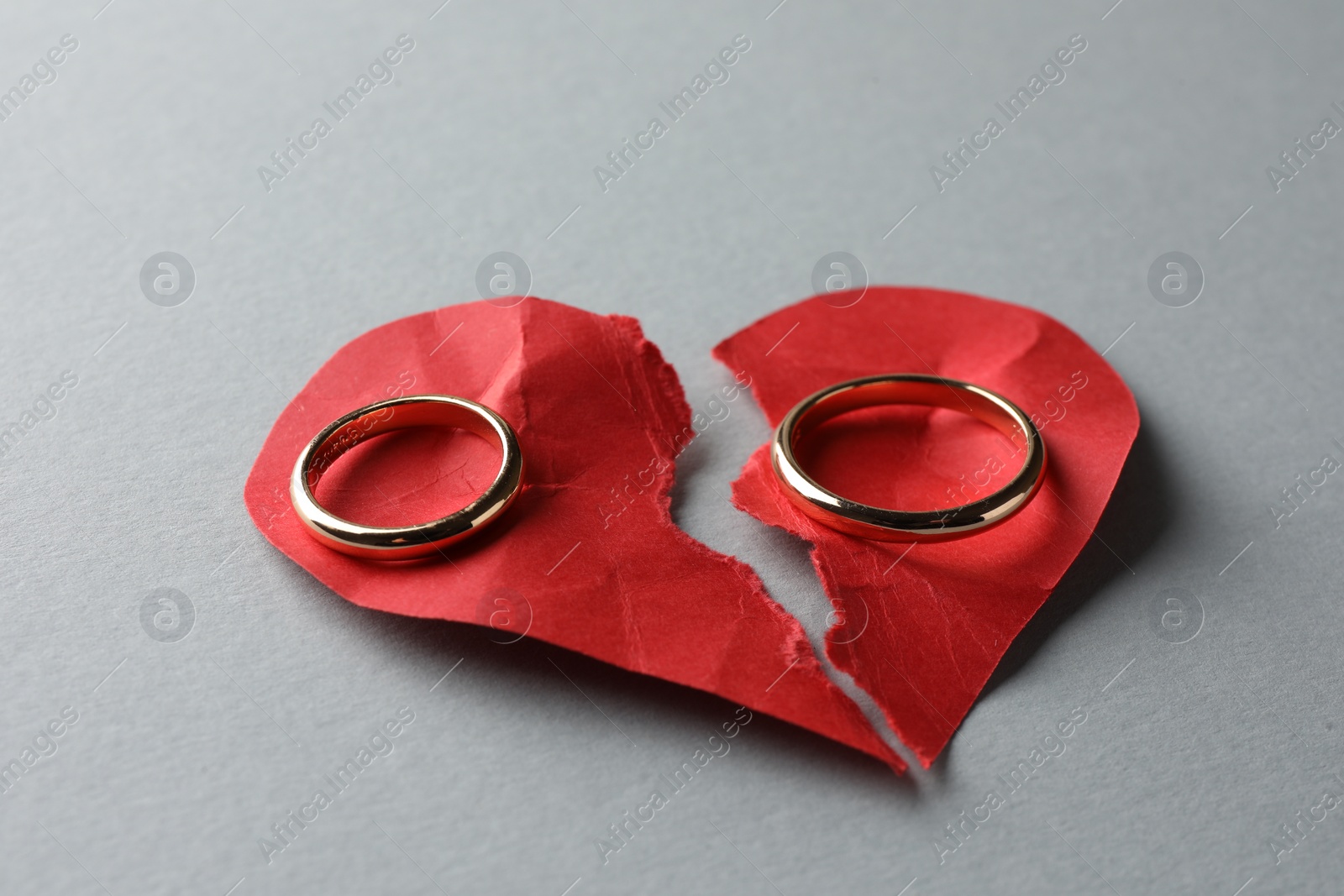 Photo of Halves of torn red paper heart and wedding rings on white background. Broken heart