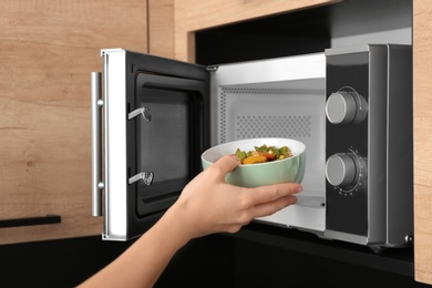 Photo of Young woman using microwave oven in kitchen