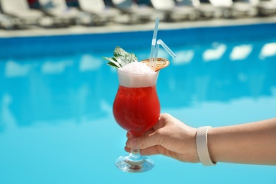 Woman with refreshing cocktail near swimming pool outdoors, closeup