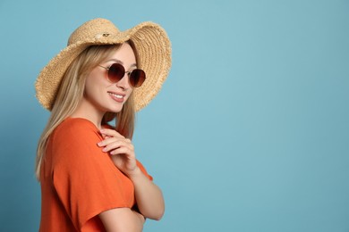 Photo of Beautiful young woman wearing straw hat and sunglasses on light blue background, space for text. Stylish headdress