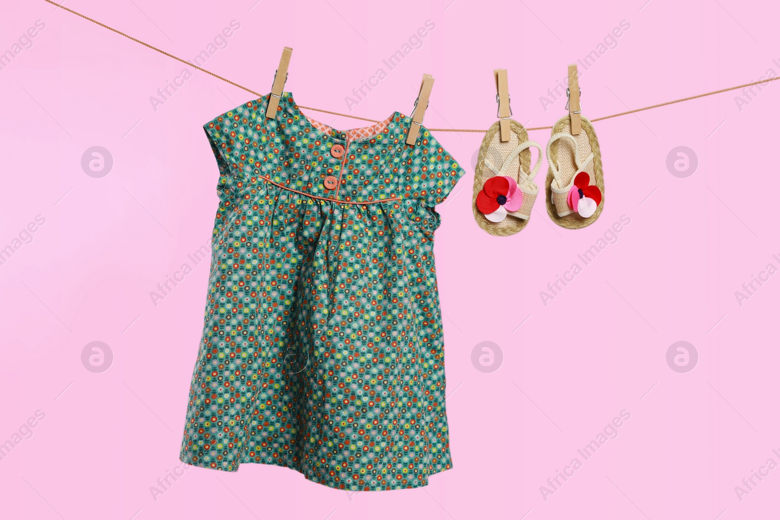 Photo of Cute baby dress and shoes drying on washing line against pink background