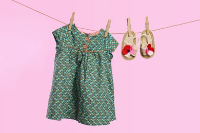 Cute baby dress and shoes drying on washing line against pink background