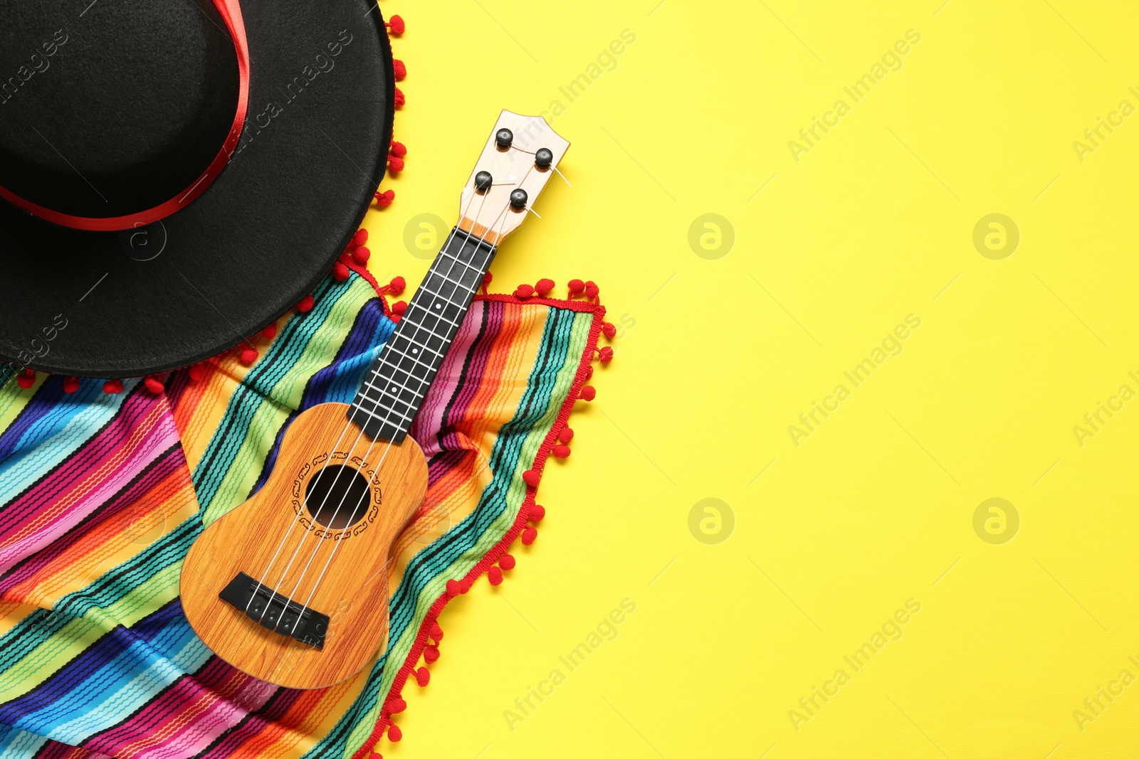 Photo of Mexican sombrero hat, guitar and colorful poncho on yellow background, flat lay. Space for text