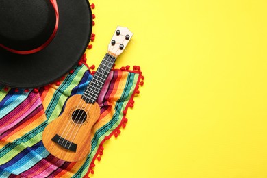 Mexican sombrero hat, guitar and colorful poncho on yellow background, flat lay. Space for text