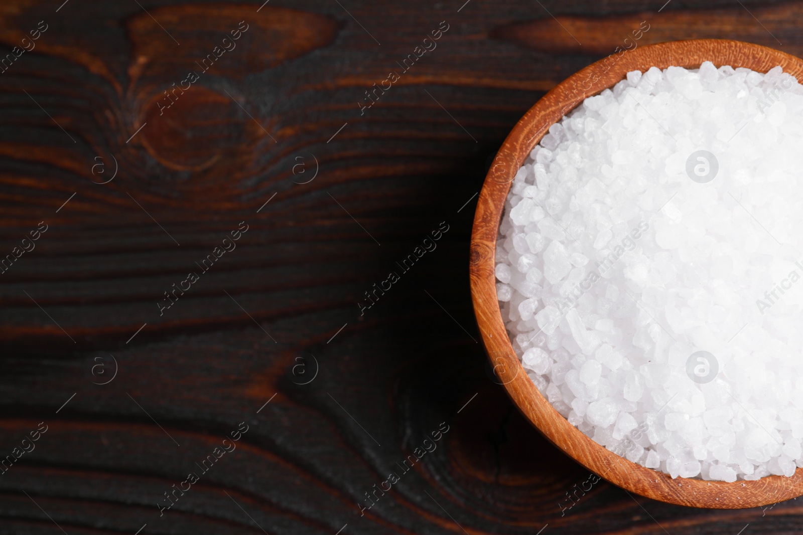 Photo of Bowl with natural sea salt on wooden table, top view. Space for text