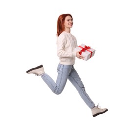 Photo of Young woman in sweater with Christmas gift jumping on white background