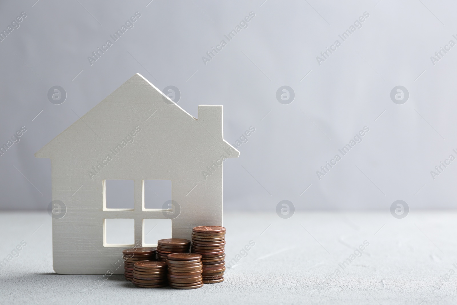 Photo of House figure and coins on table against light background. Space for text