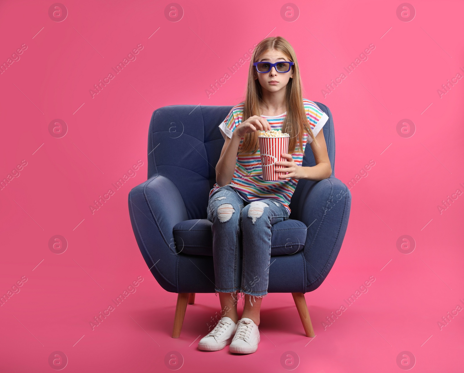 Photo of Emotional teenage girl with 3D glasses and popcorn sitting in armchair during cinema show on color background