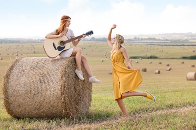 Photo of Beautiful hippie woman dancing while her friend playing guitar in field, space for text