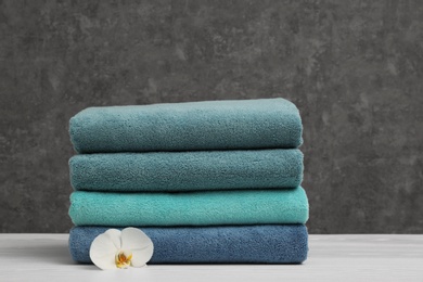 Stack of soft clean towels with beautiful flower on table. Space for text