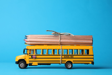 Photo of School bus model with color pencils on light blue background. Transport for students