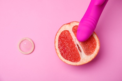 Photo of Half of grapefruit, purple vibrator and condom on pink background, flat lay. Sex concept