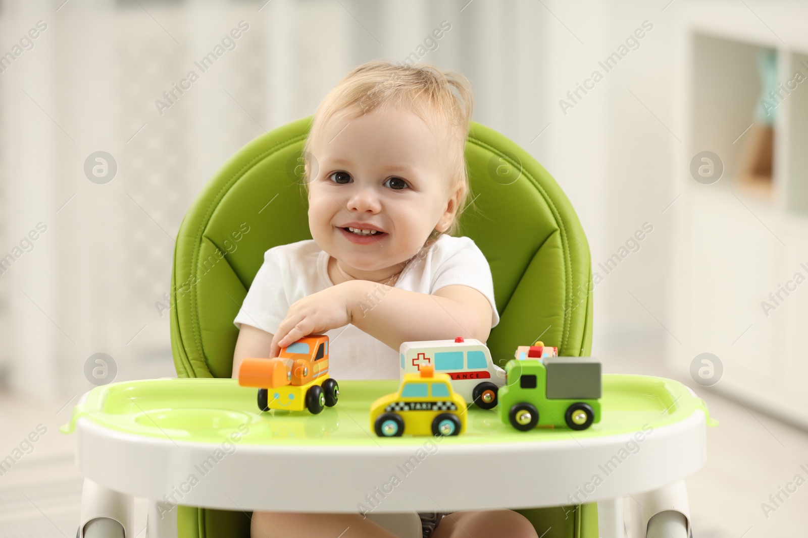 Photo of Children toys. Cute little boy playing with toy cars in high chair at home