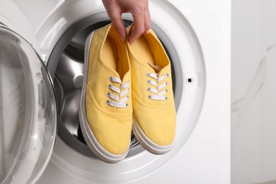 Woman putting pair of sport shoes into washing machine, closeup