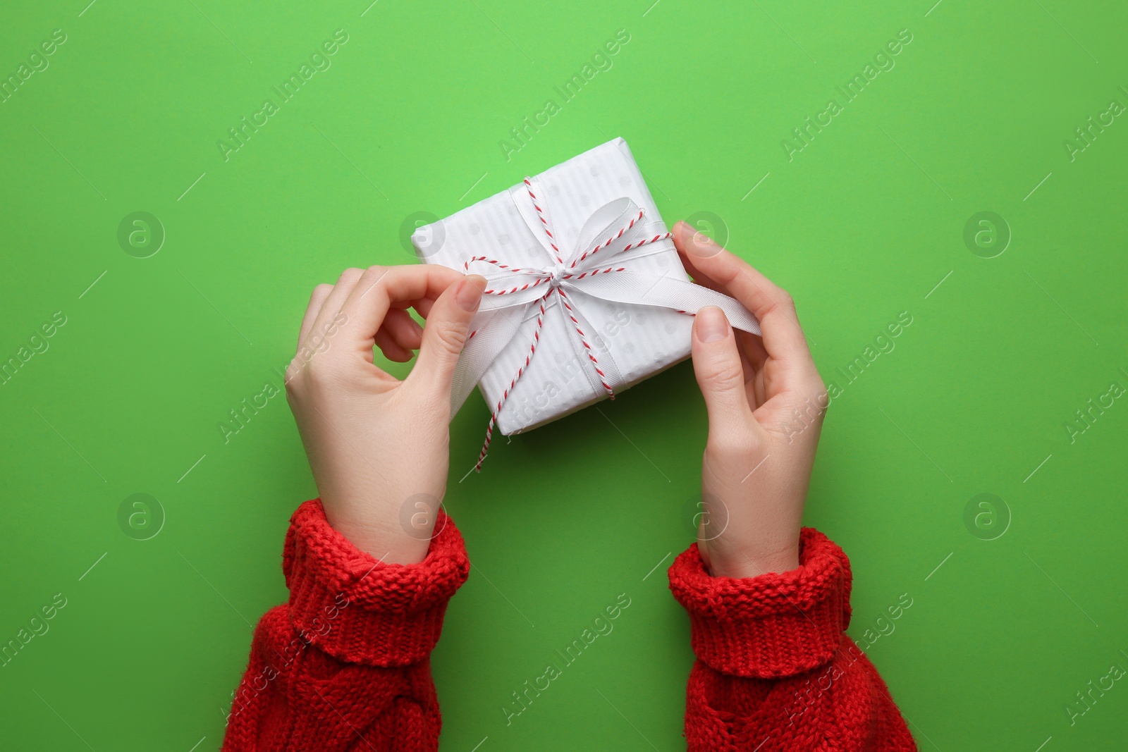 Photo of Woman holding Christmas gift box on green background, top view