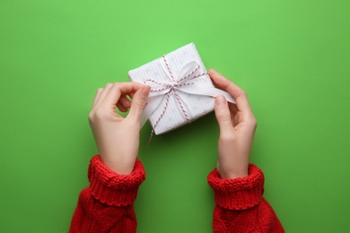 Woman holding Christmas gift box on green background, top view