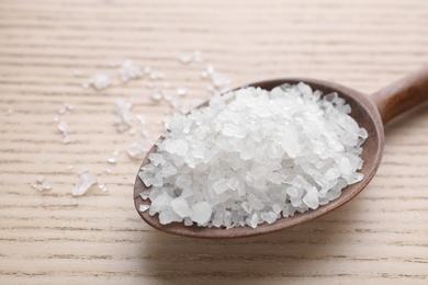 Photo of Spoon with white sea salt on wooden table, closeup. Spa treatment