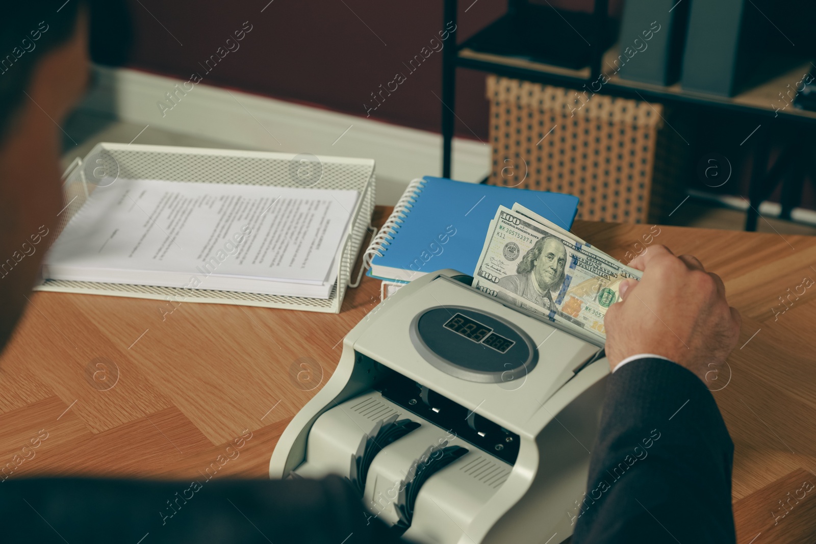 Photo of Man putting money into banknote counter at wooden table indoors, closeup