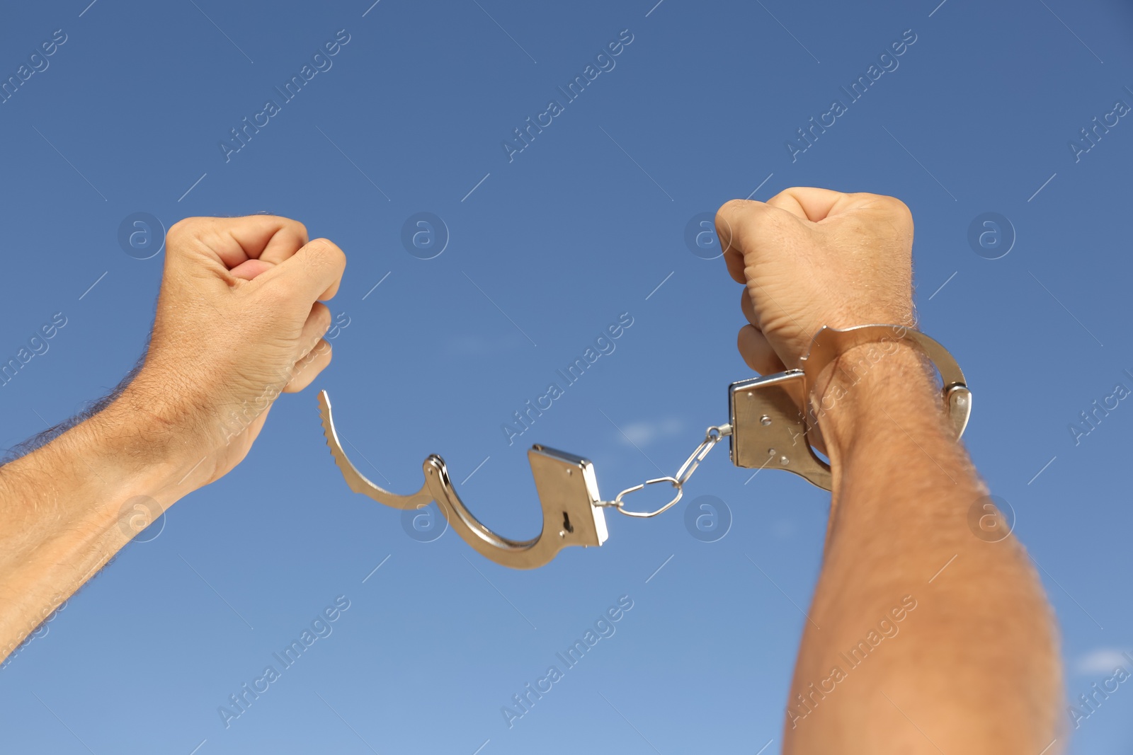 Photo of Man in handcuffs against blue sky outdoors, closeup