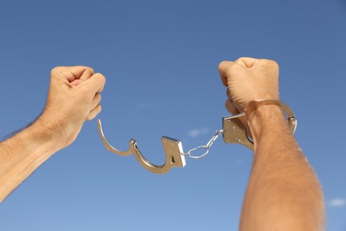 Photo of Man in handcuffs against blue sky outdoors, closeup