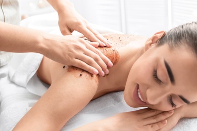 Young woman having body scrubbing procedure in spa salon, closeup