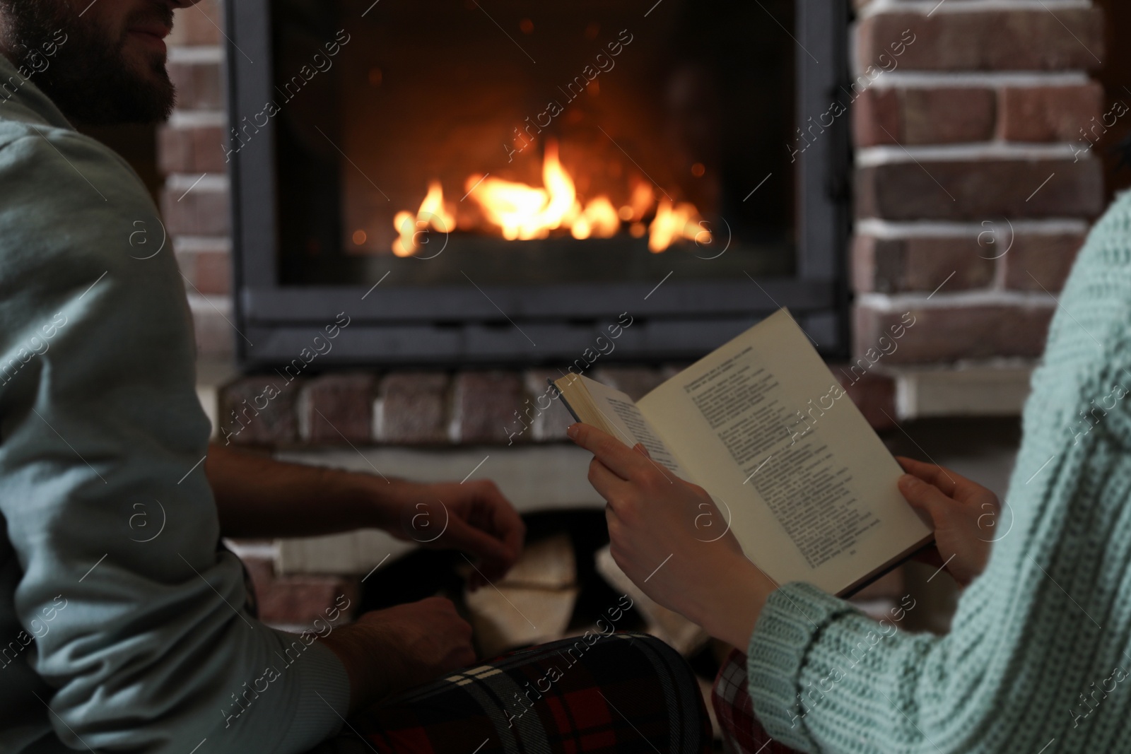 Photo of Couple reading book near burning fireplace at home, closeup