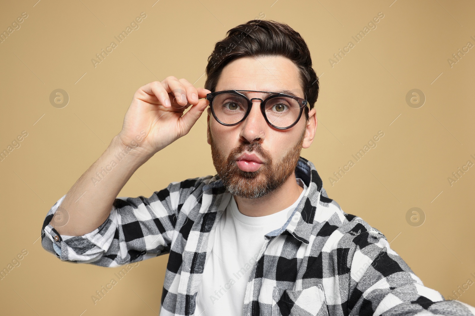 Photo of Handsome man taking selfie while blowing kiss on beige background