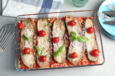 Flat lay composition with baked eggplant, tomatoes and basil in dishware on table