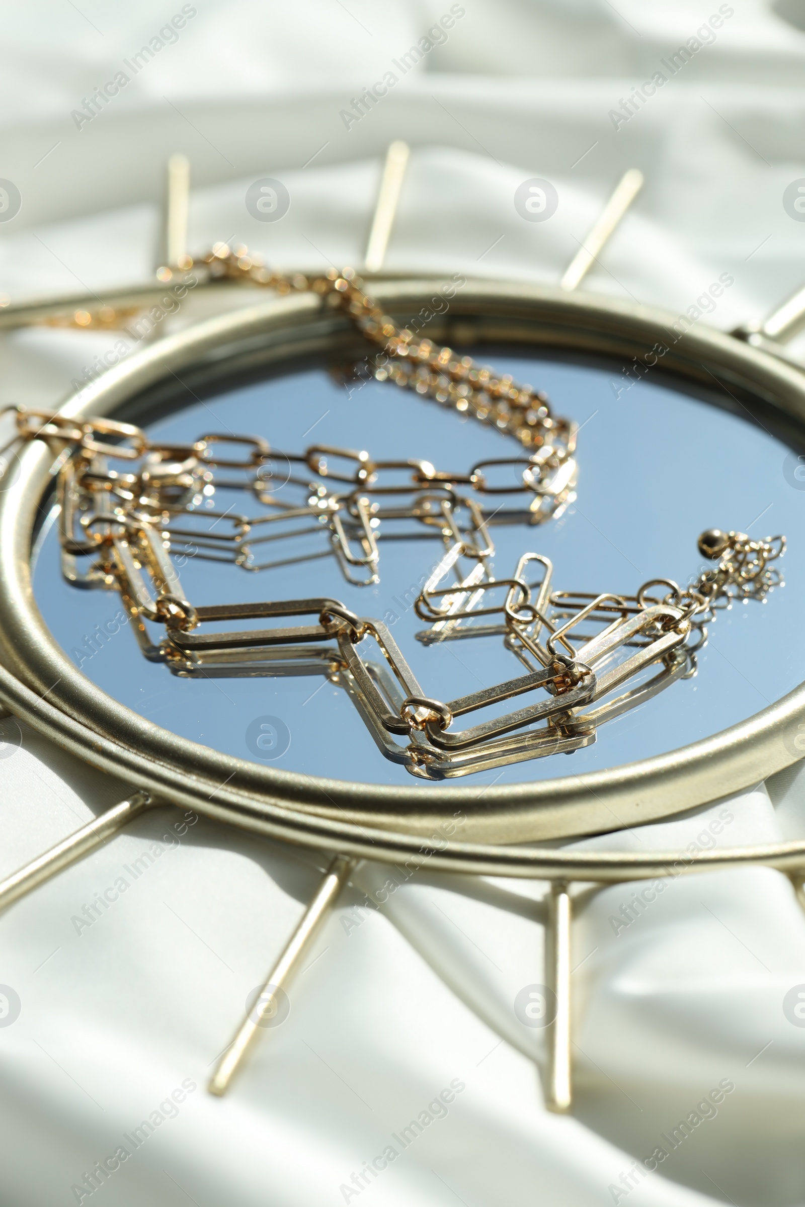 Photo of Metal chains and mirror on white fabric, closeup. Luxury jewelry