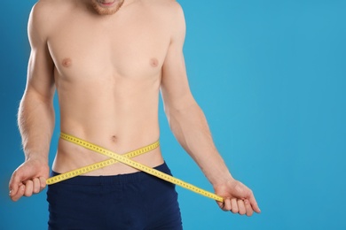 Man with slim body measuring his waist on color background, closeup. Space for text