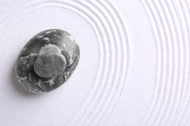 Photo of Zen garden stones on white sand with pattern, top view. Space for text