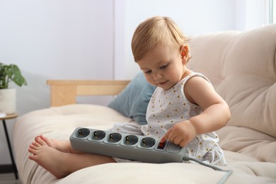 Cute baby playing with power strip on sofa at home. Dangerous situation
