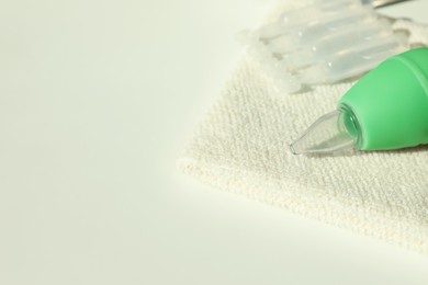 Single dose ampoules of sterile isotonic sea water solution, towel and nasal aspirator on white table, closeup. Space for text