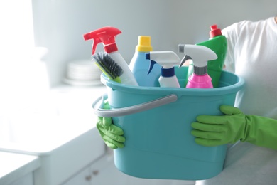 Woman holding bucket with cleaning supplies in kitchen, closeup