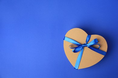 Photo of Beautiful heart shaped gift box with bow on blue background, top view. Space for text