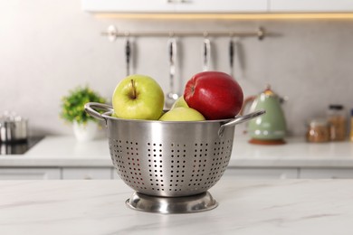 Photo of Colander with fresh apples on white marble table in kitchen