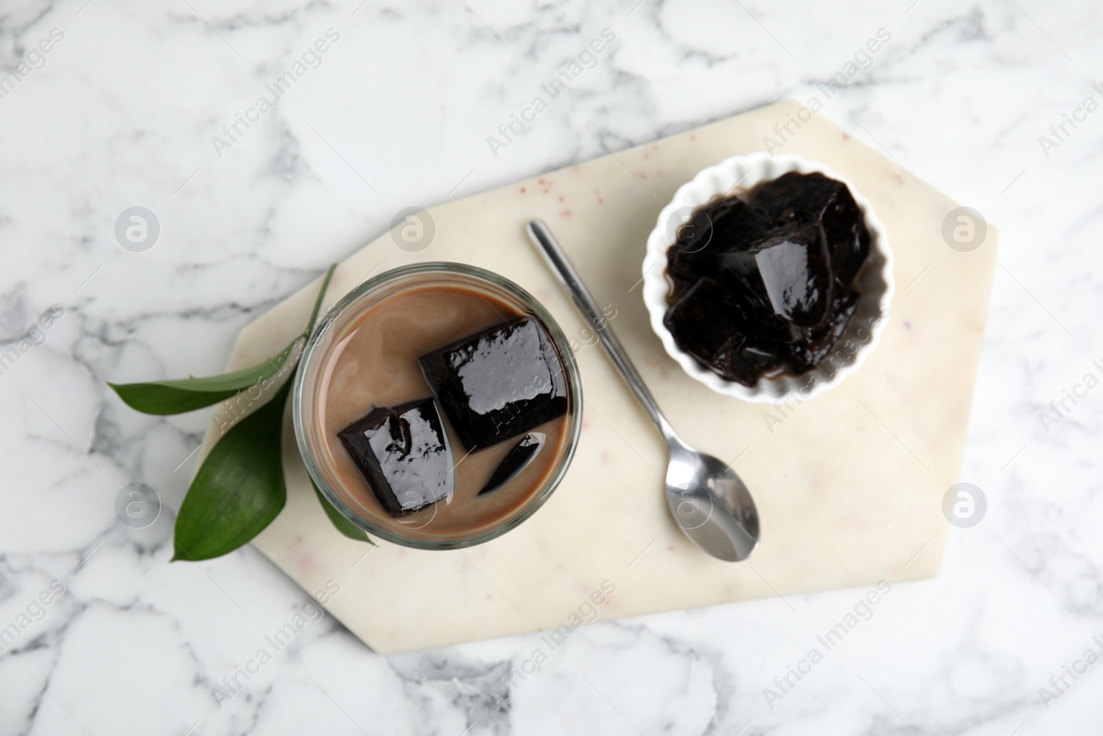 Photo of Glass of milk with grass jelly on white marble table, top view