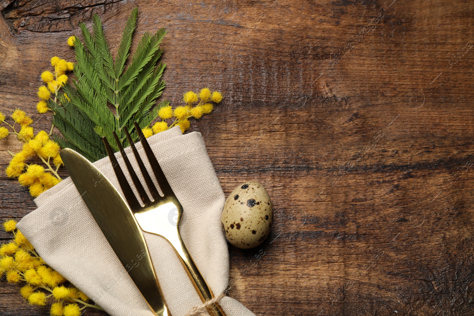 Photo of Top view of cutlery set with quail egg and floral decor on wooden table, space for text. Easter celebration