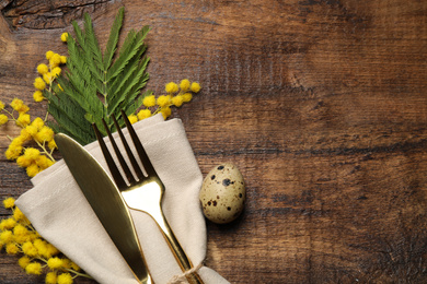 Top view of cutlery set with quail egg and floral decor on wooden table, space for text. Easter celebration