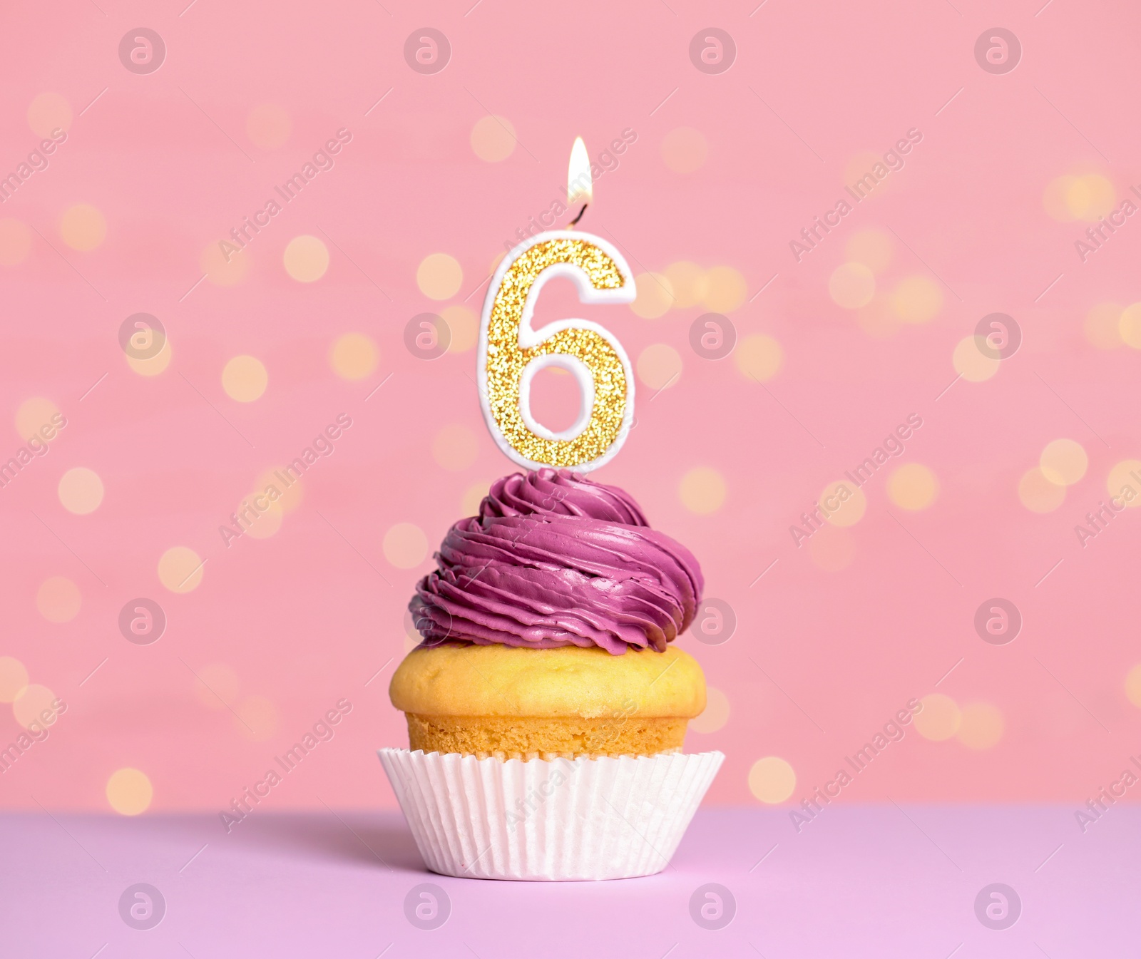 Photo of Birthday cupcake with number six candle on table against festive lights