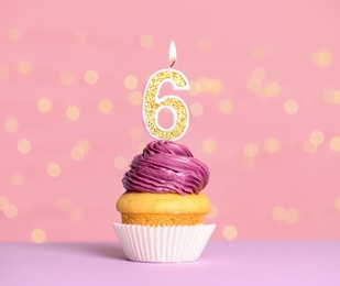 Photo of Birthday cupcake with number six candle on table against festive lights