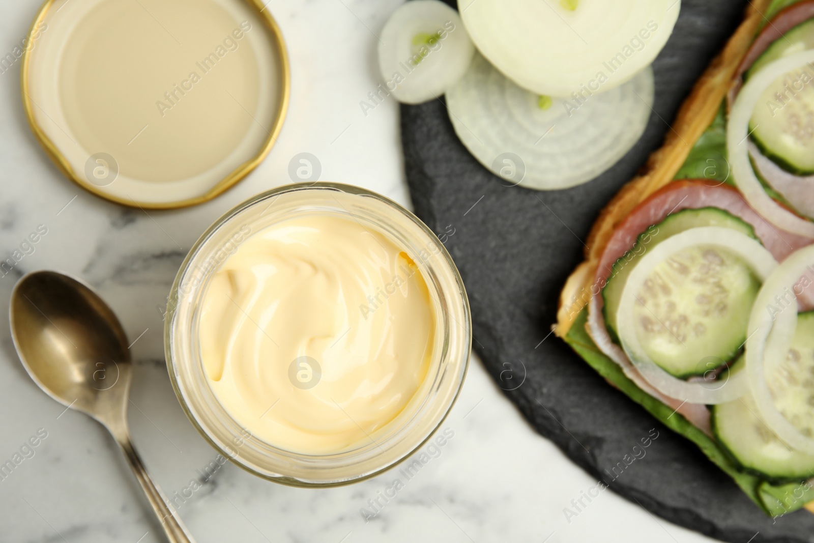 Photo of Jar of delicious mayonnaise near fresh sandwich on white marble table, flat lay
