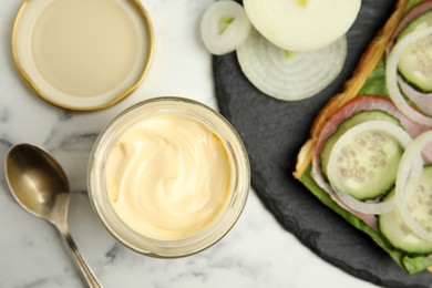 Jar of delicious mayonnaise near fresh sandwich on white marble table, flat lay