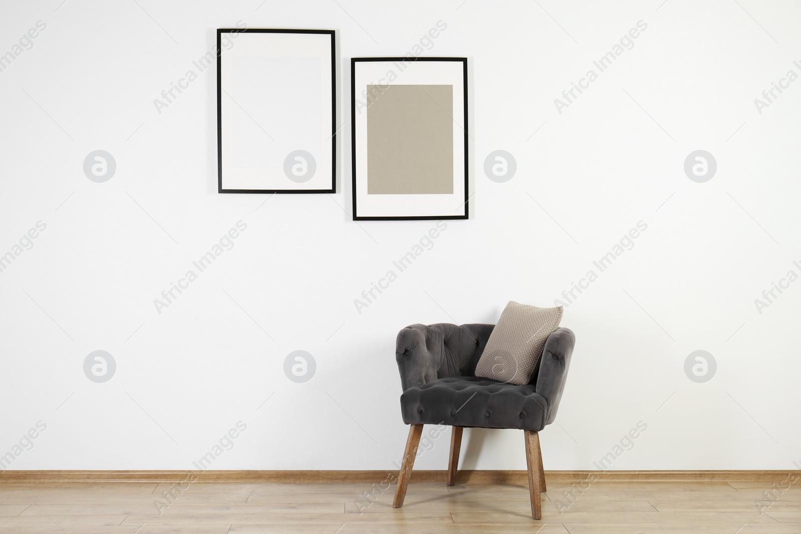 Photo of Comfortable armchair, cushion and frames in room with white wall. Interior design